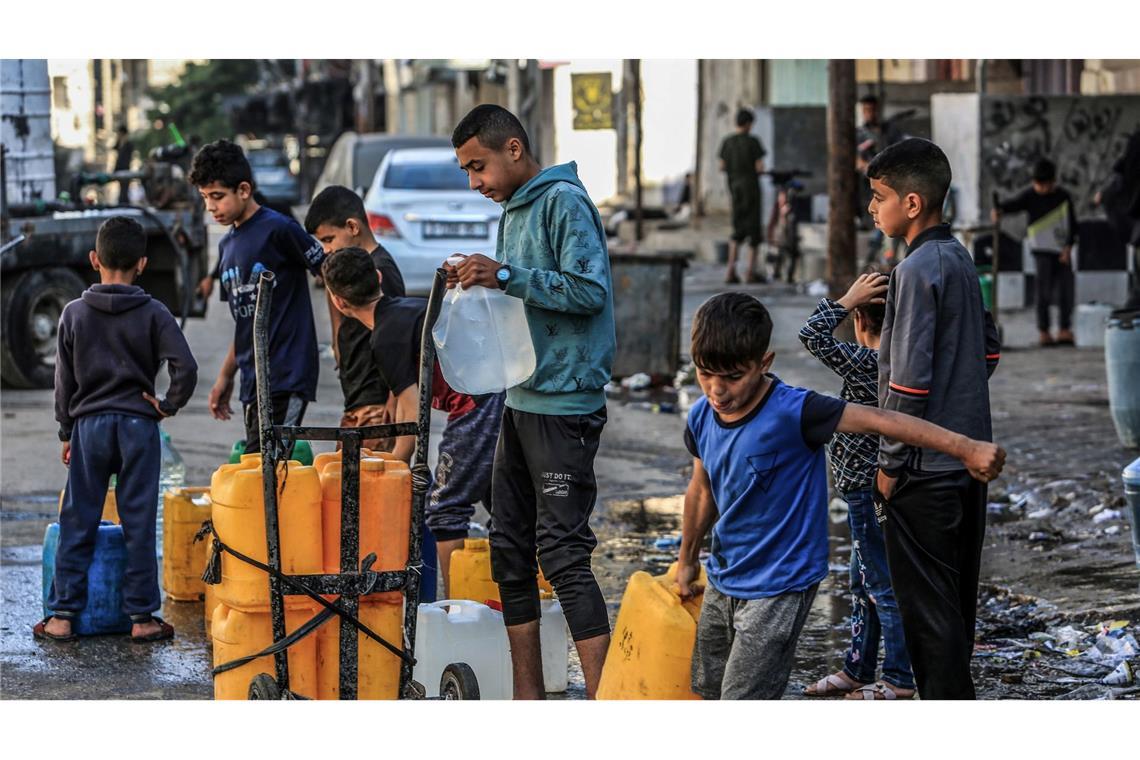 Palästinensische Kinder stehen mit Wasserbehältern Schlange, um sie mit Trinkwasser zu füllen.